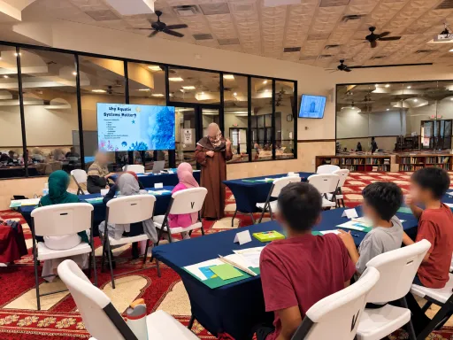 Children at tables in a masjid hall, facing a teacher beside a slide titled Why Aquatic Systems Matter?