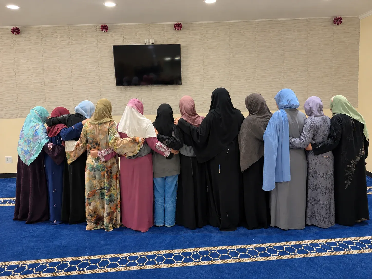 Women standing arm in arm in a masjid hall